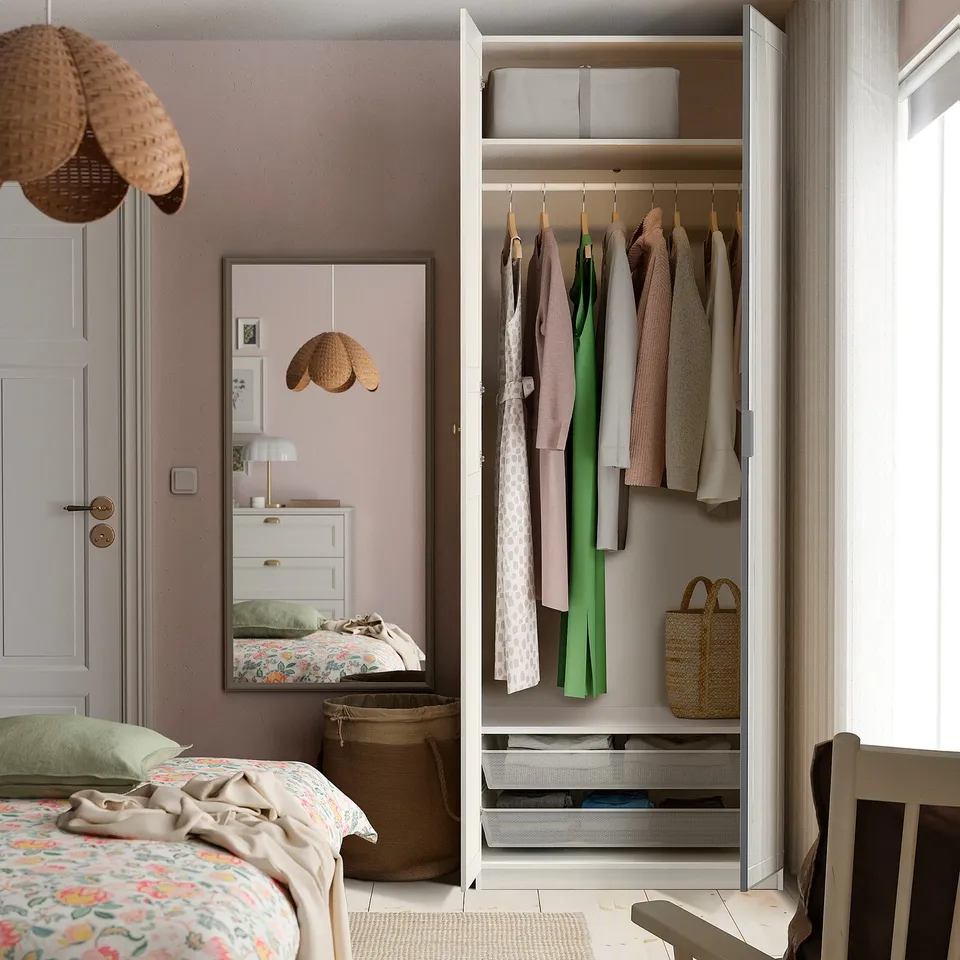 Open PAX wardrobe with clothes and storage against pink wall.