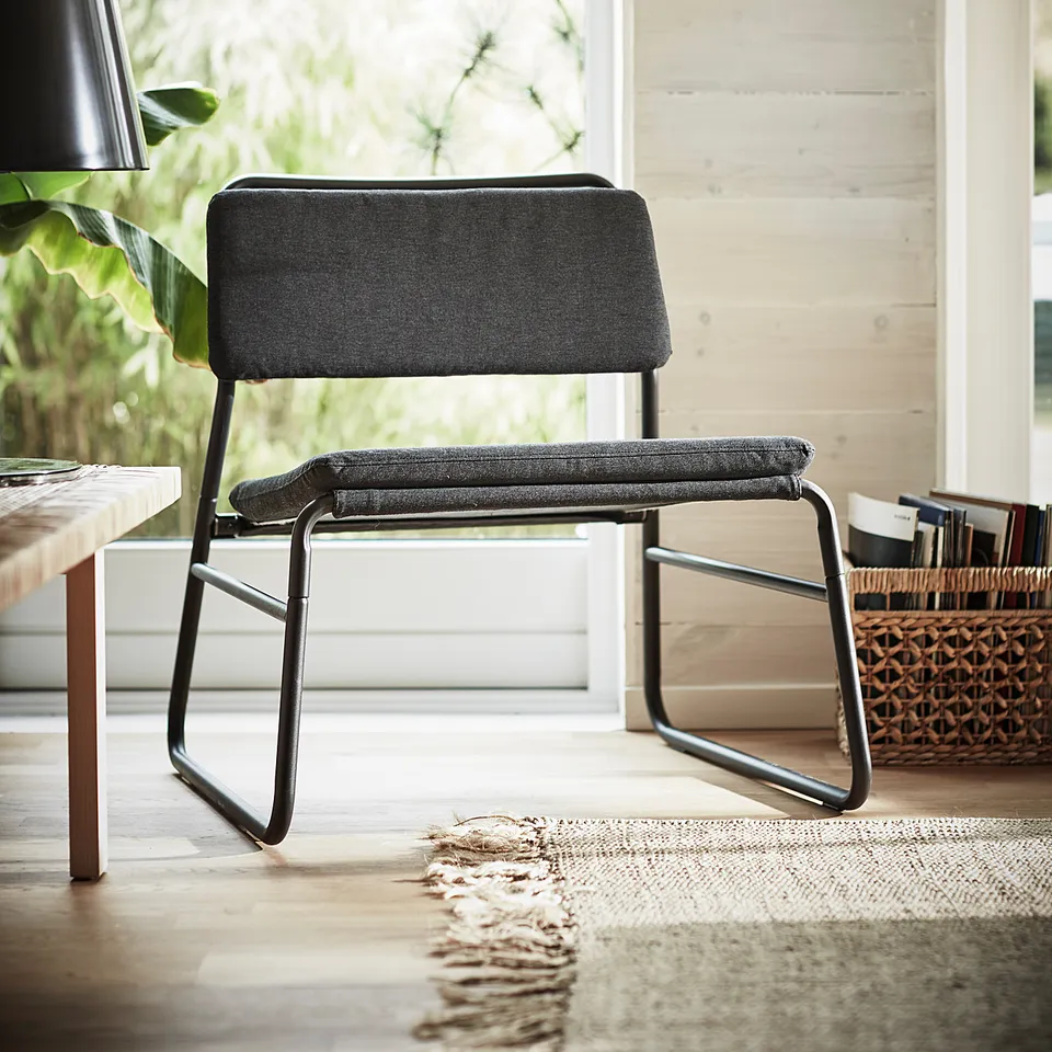 Modern grey chair with metal frame, cushioned seat and back, positioned near a window.