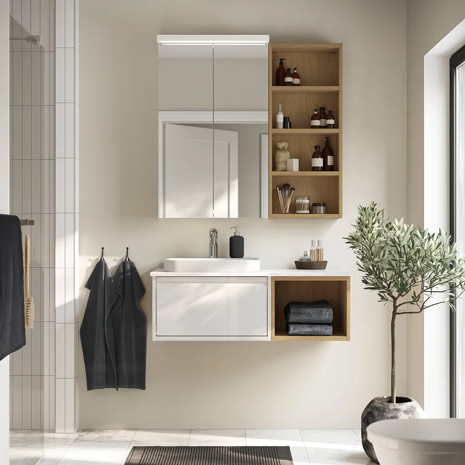 Modern bathroom with white floating ÄNGSJÖN vanity, sleek sink, mirror cabinet, and wooden shelves. Grey towels hang beside it.
