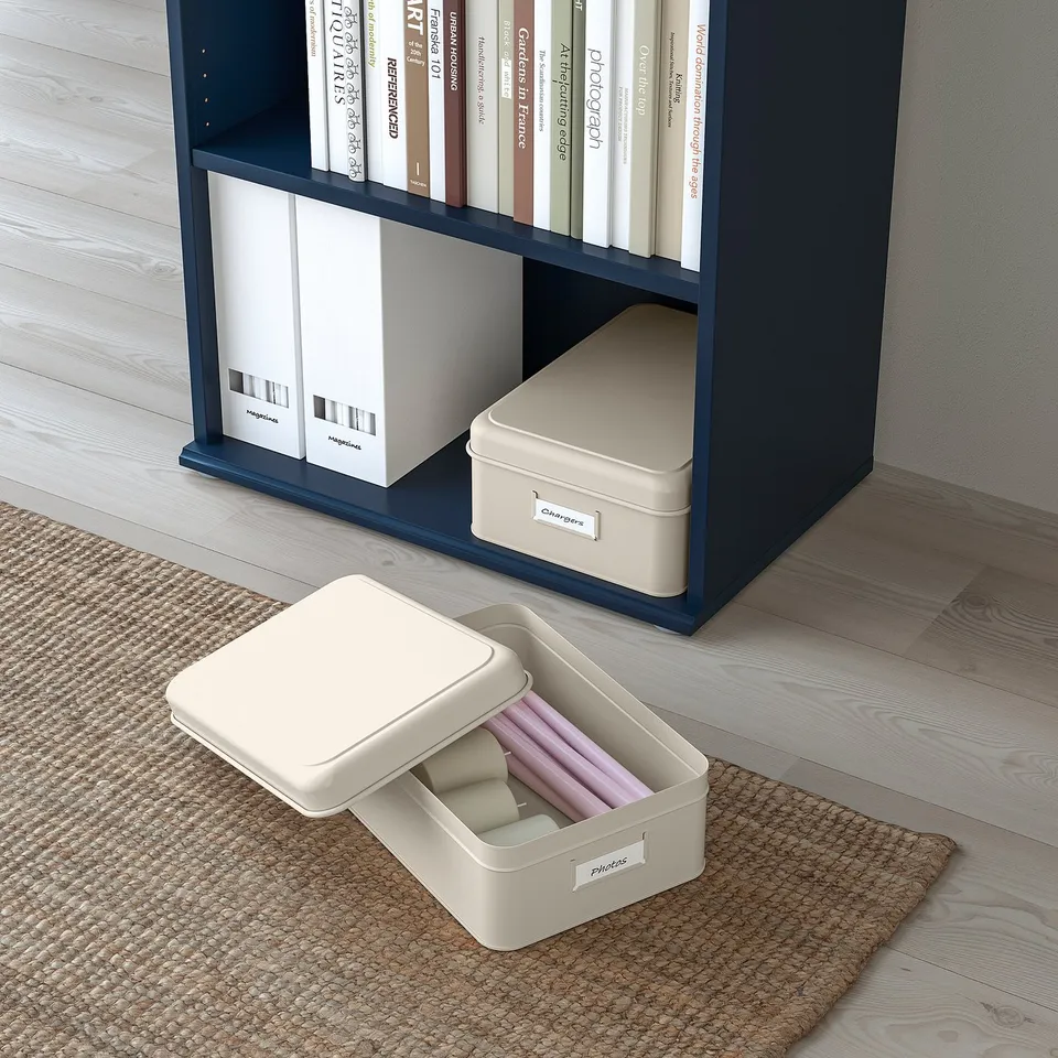 Bookshelf with blue shelves holding white-organizer boxes and labelled containers, some open revealing contents.