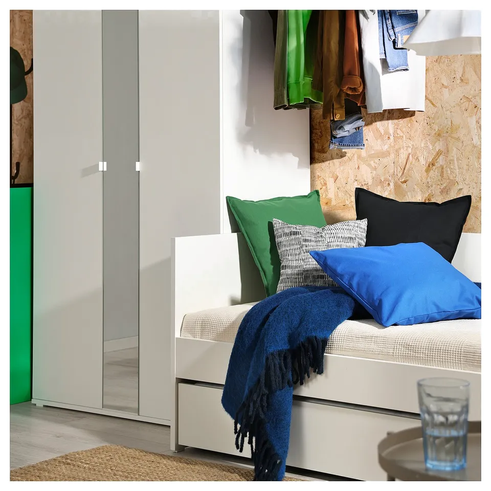 A modern white daybed with colourful pillows and a blue blanket, near a closet.