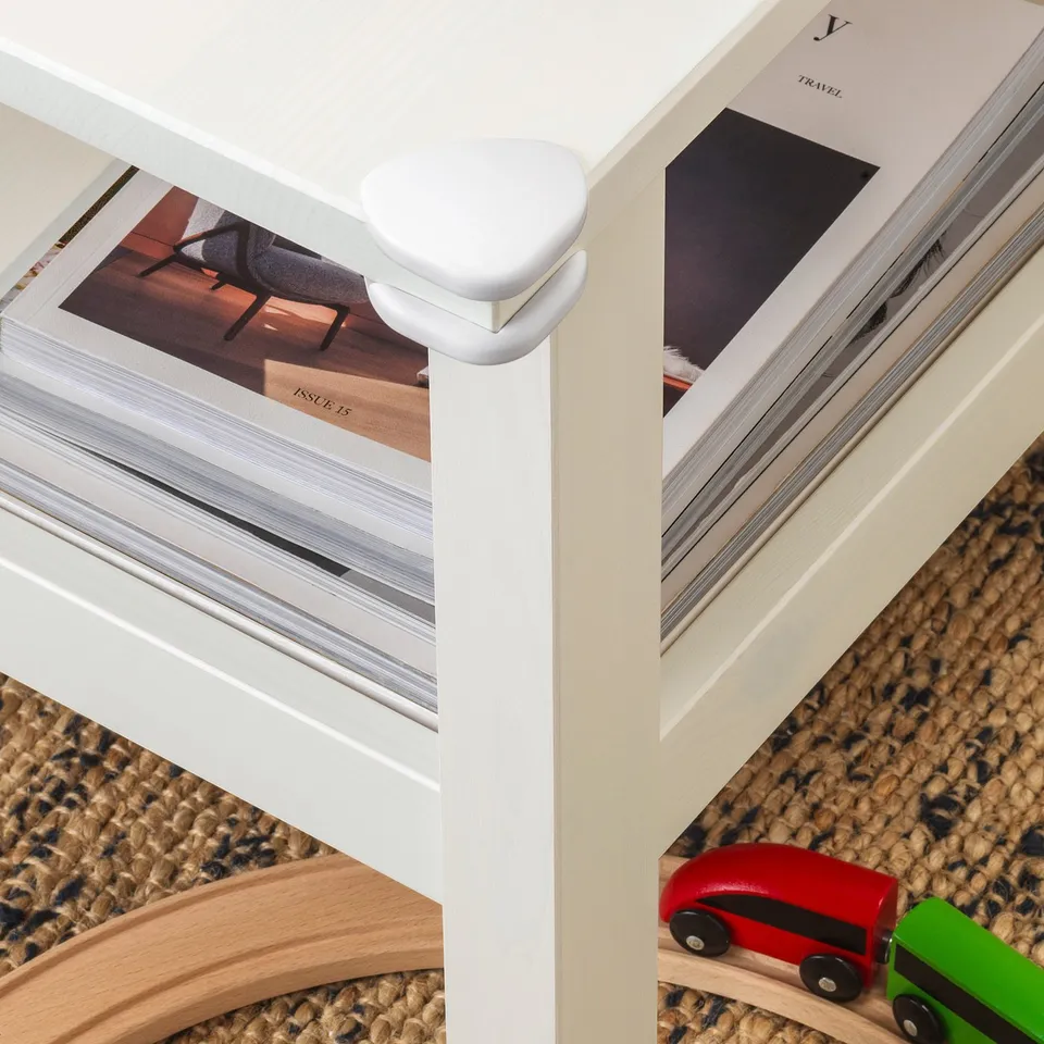 White corner bumpers on table edges for child safety. Magazines and toy cars on table.