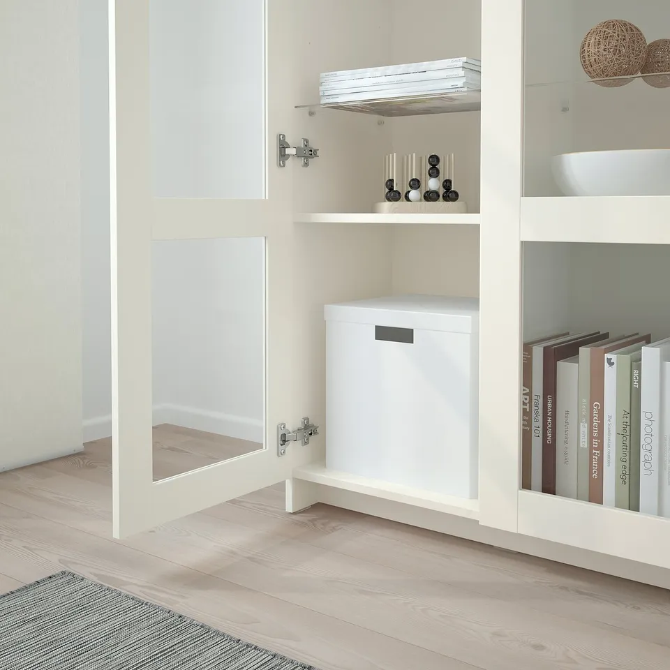 A white cabinet with glass doors, holding books and decorative items, featuring adjustable shelves and protective glass panels.
