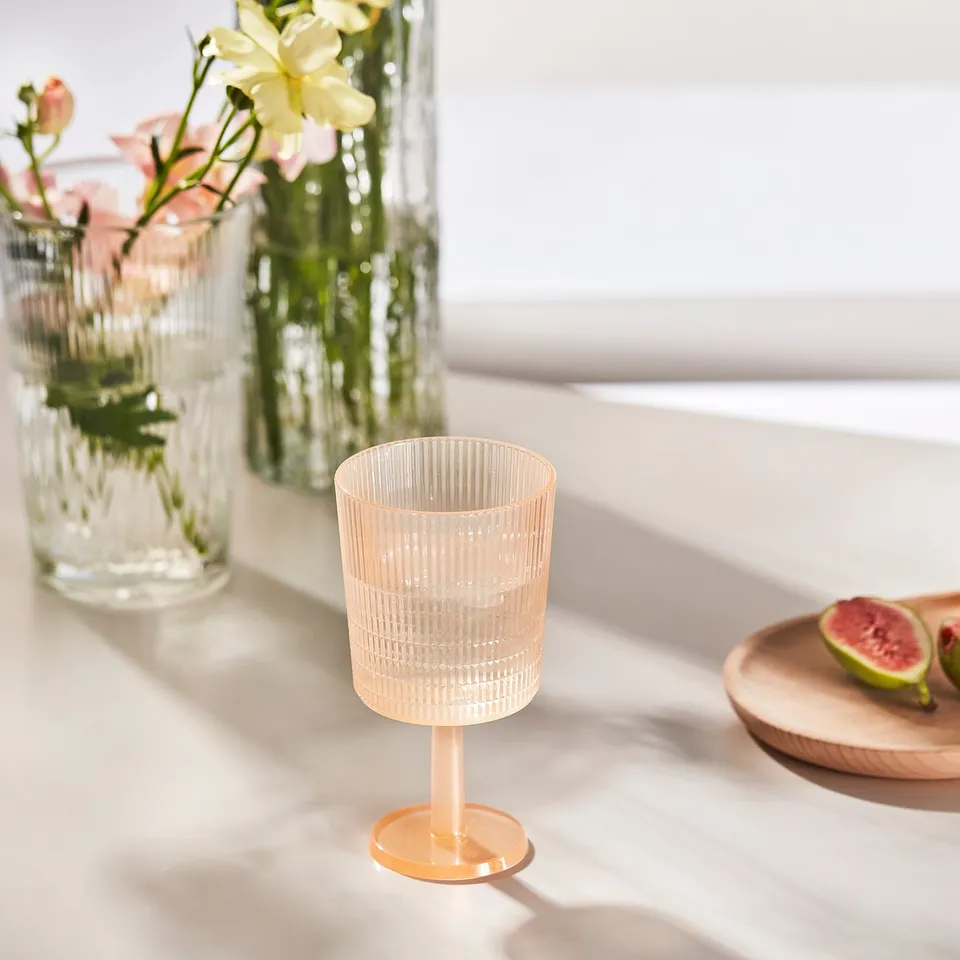 An orange KALLSINNIG glass sits beside vases with flowers on a white table.