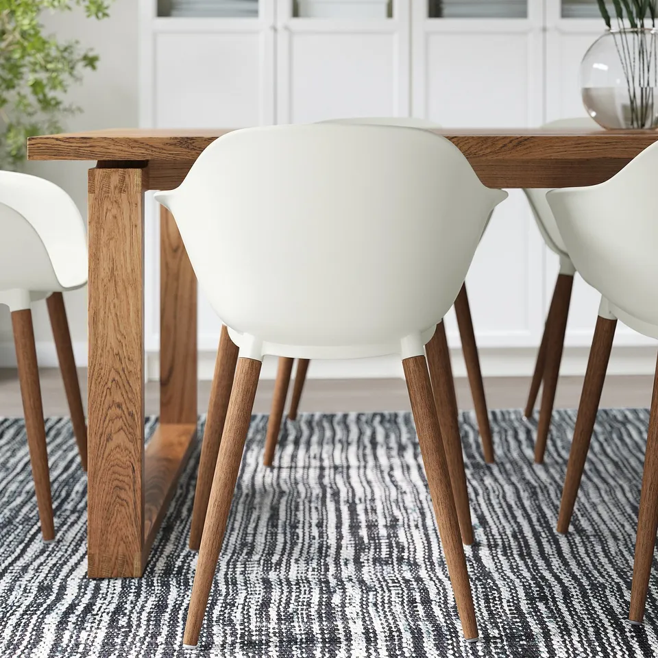 Modern dining set with white chairs and wooden table on a patterned rug. Easy to clean and durable.