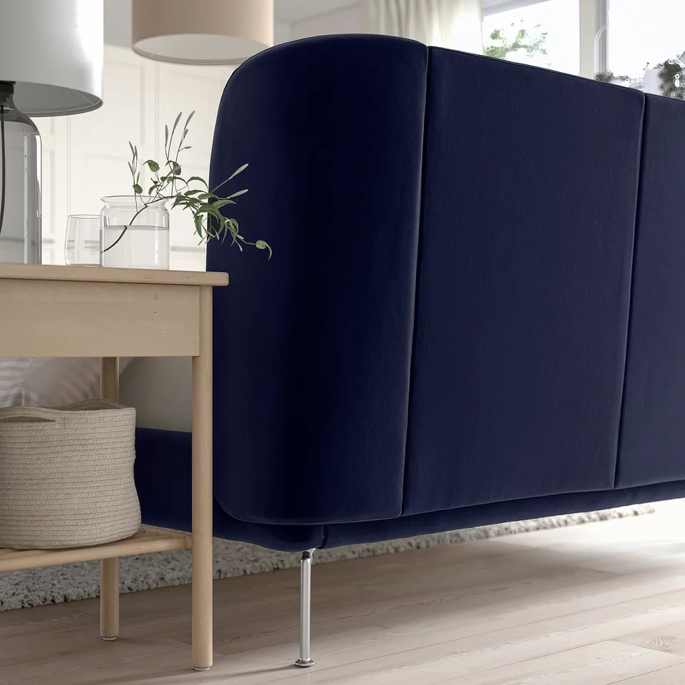 A dark blue TUFJORD bed with a curved, upholstered headboard, and a wooden side table with a plant.