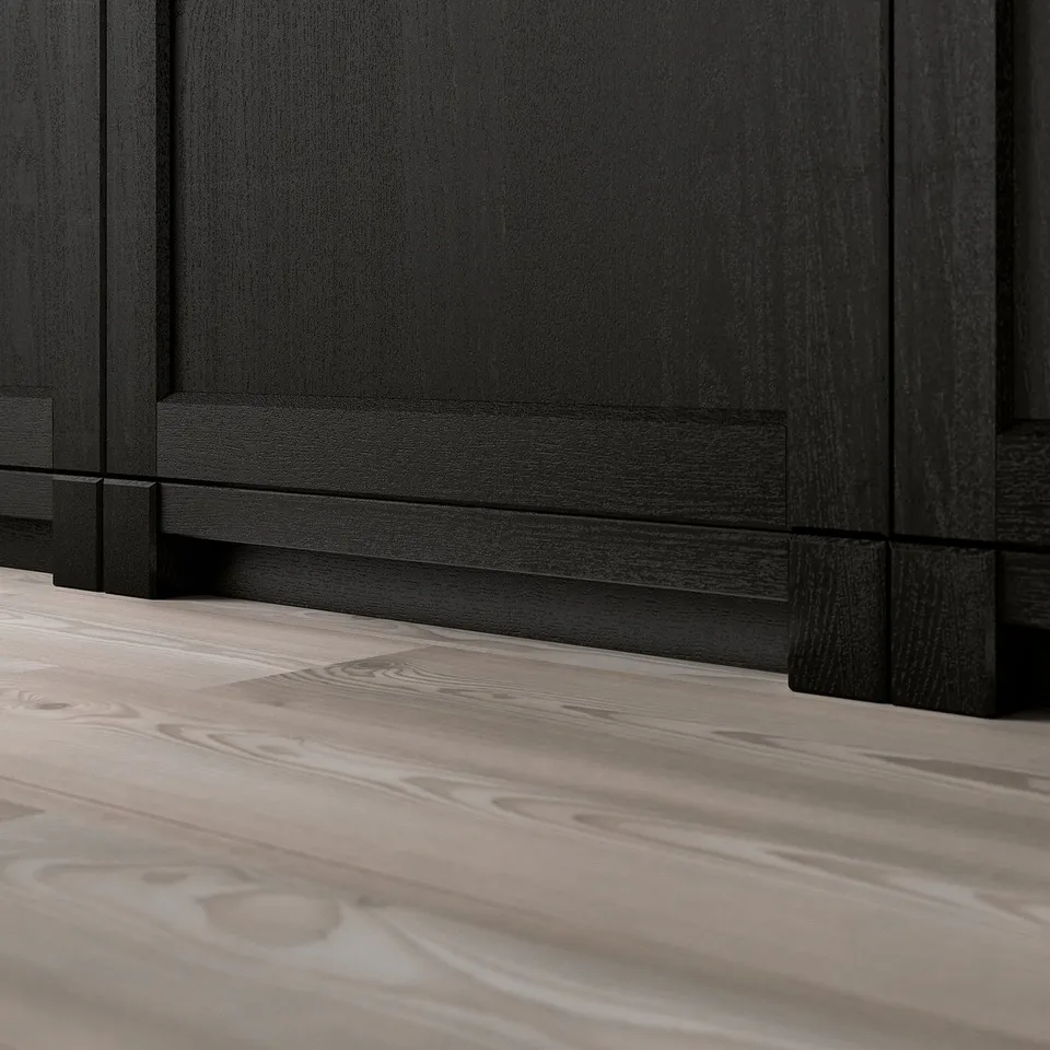 Dark wooden kitchen cabinets with a bevelled edge base panel on a light wooden floor.