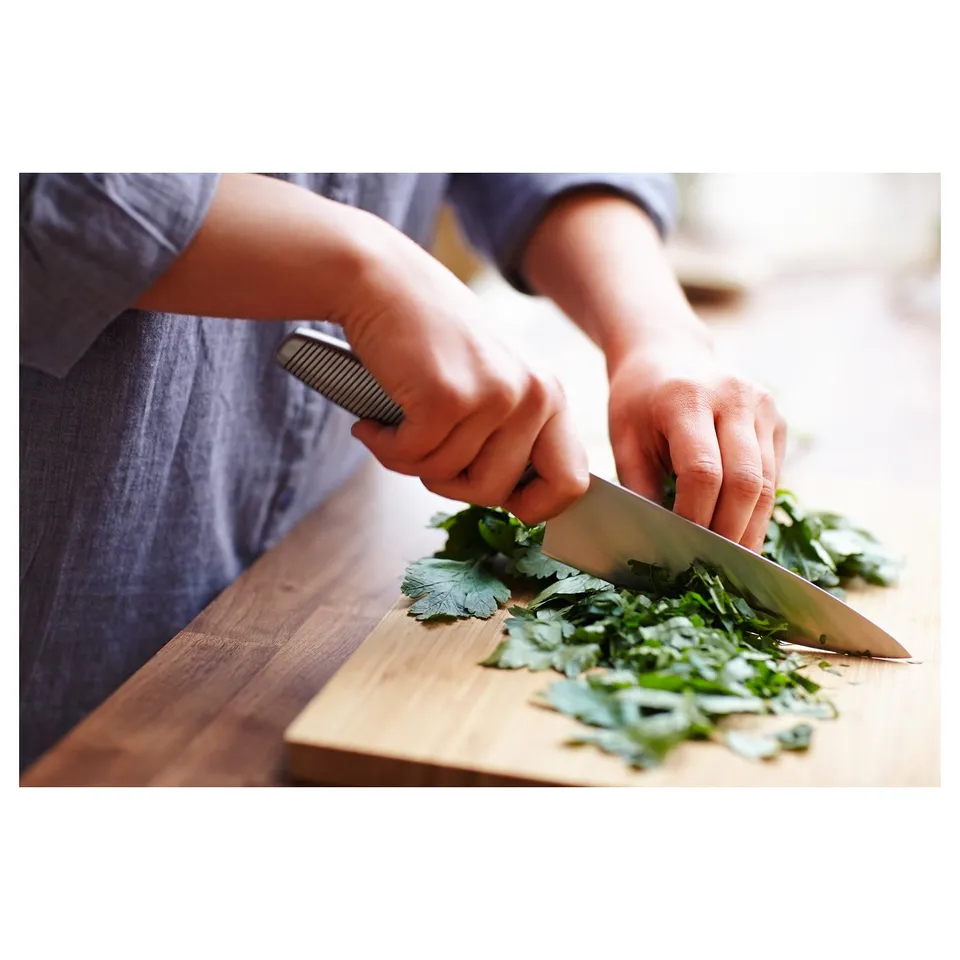 A person is chopping leafy greens on a wooden cutting board with a sharp stainless steel knife, showcasing its cutting efficiency.