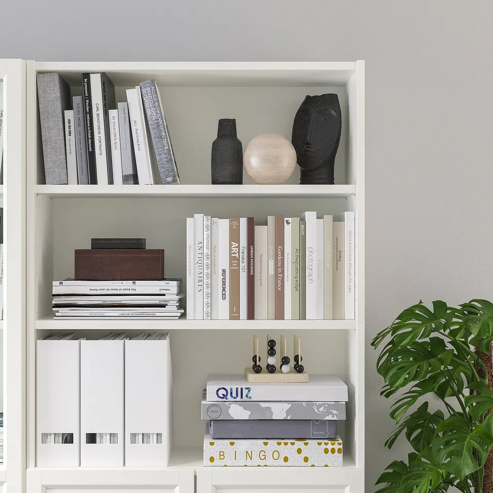 A white bookshelf with adjustable shelves holding books and decor items.