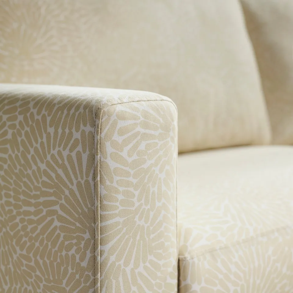 Close-up of upholstered sofa corner, showing high-quality, patterned fabric and detailed stitching.
