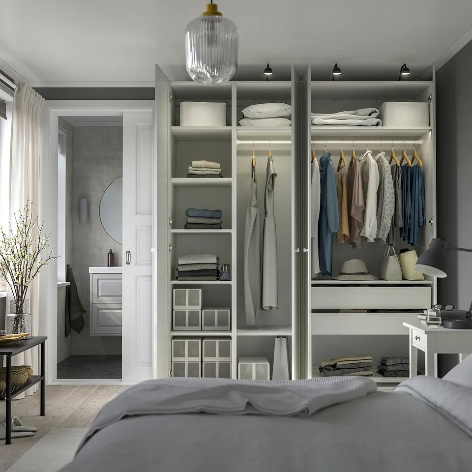 Modern bedroom with open closet, clothes, textiles, drawers, and lighting. Bed and plant in foreground.