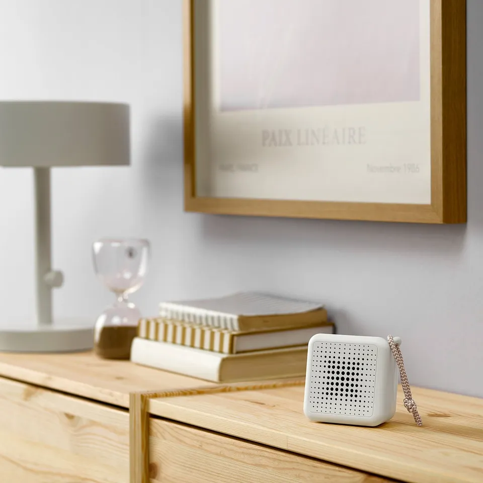 Small white VAPPEBY speaker on table with books, lamp, and hourglass.