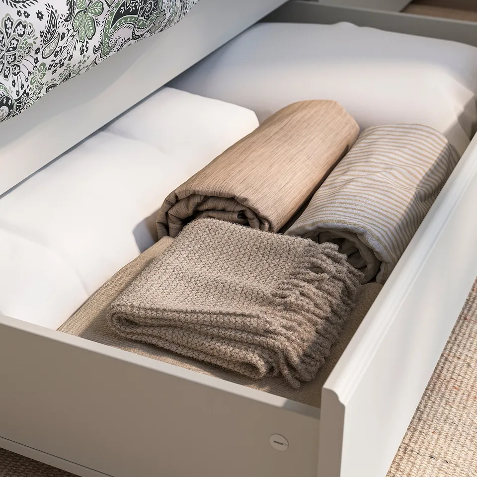 Open drawer of FÅGELFJÄLLET bed, showing neatly folded blankets and pillows, highlighting storage feature.