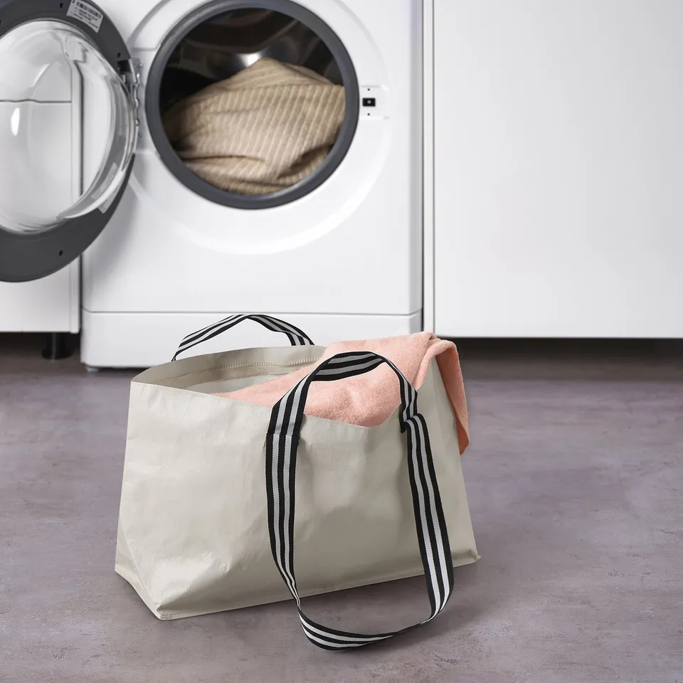 White laundry bag with black stripes resting on floor near dryer, used for carrying clothes.