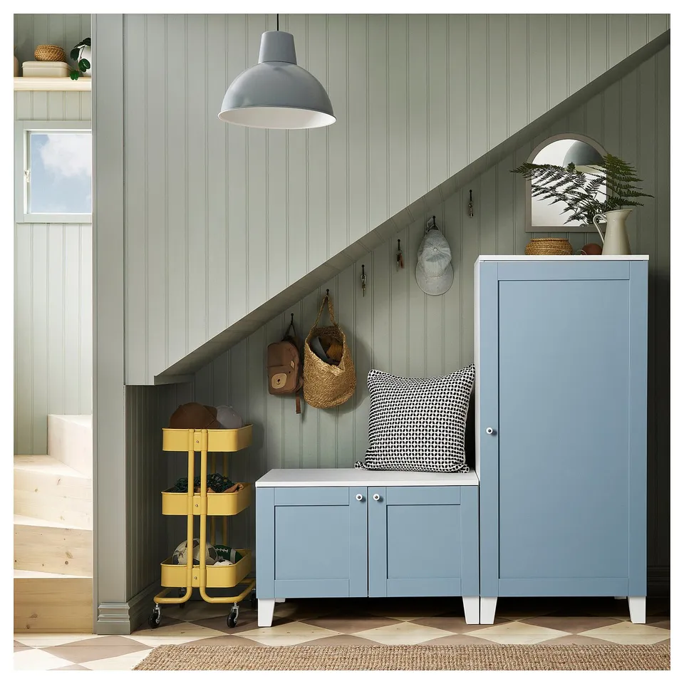 Blue SANNIDAL cabinet under stairs, yellow trolley, grey bench with pillow, grey wall, hanging items, grey pendant lamp.