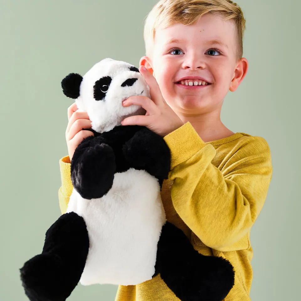 A boy smiles, holding a black and white panda stuffed toy. The panda has large ears and arms, and the boy wears a yellow shirt.