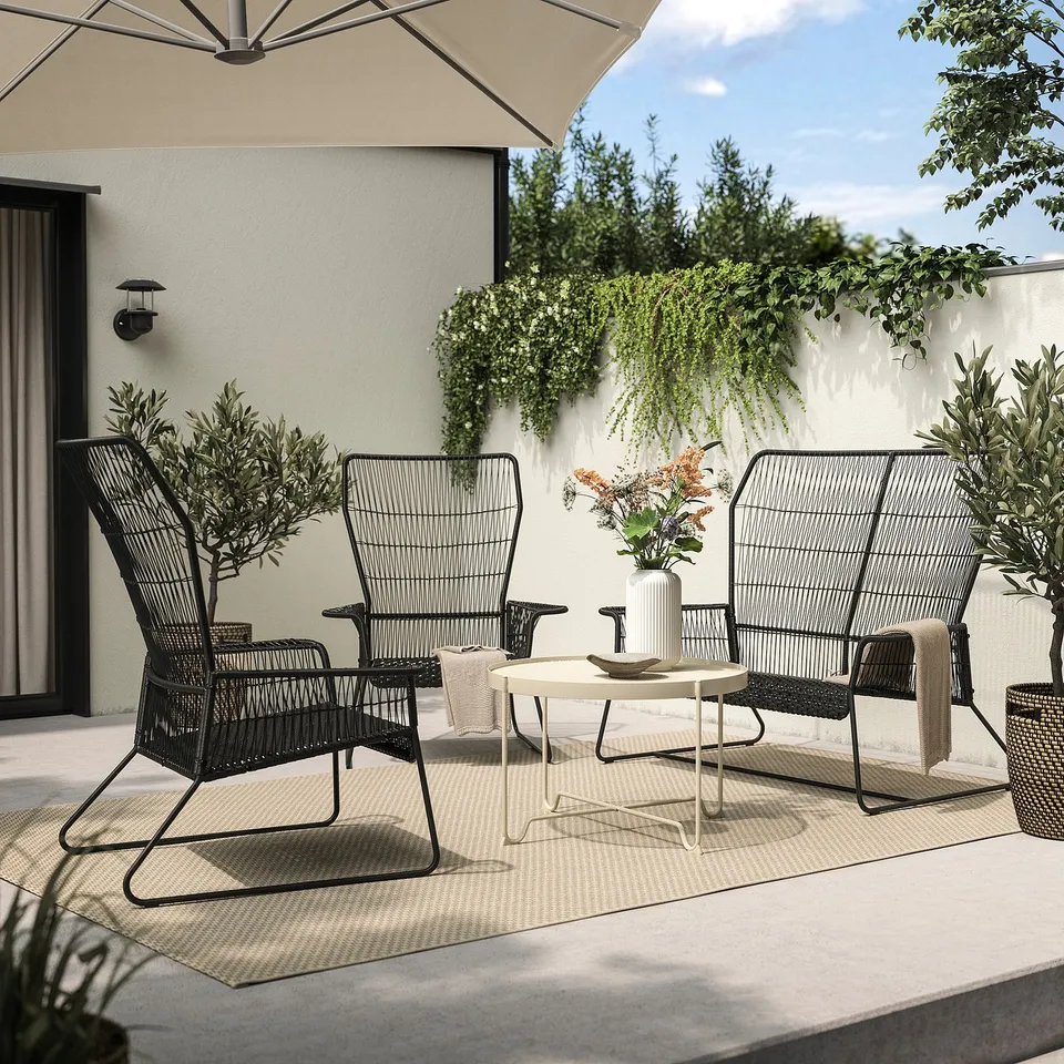 Modern outdoor seating area with black wicker chairs and white coffee table, under beige umbrella, on a light-colored rug.