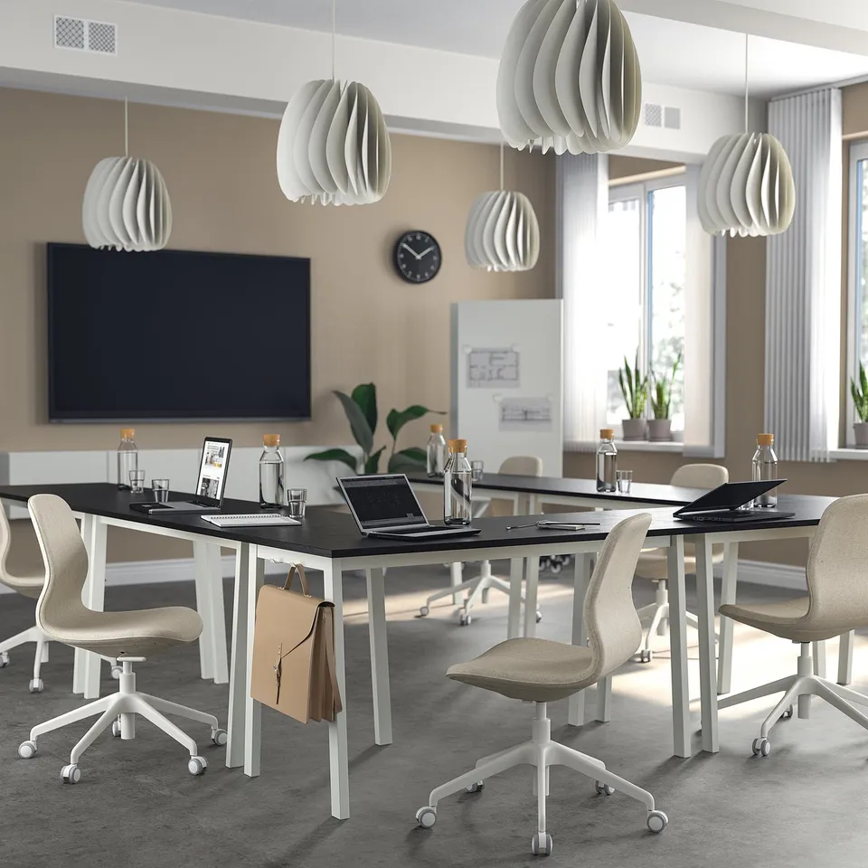 Modern office with MITTZON tables, chairs & lamps, flat-screen tv, clock, plants, natural light.