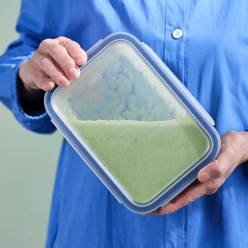 Person holding green smoothie in clear IKEA glass container.