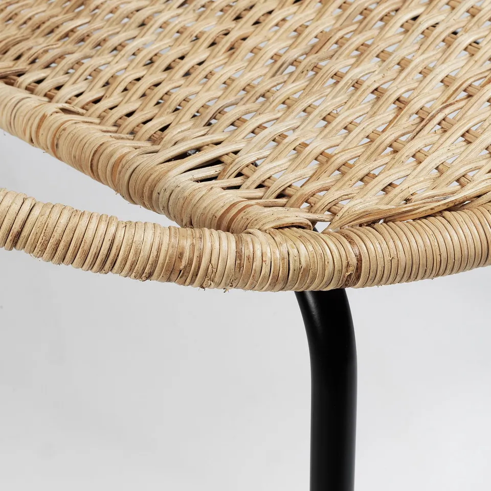 Wicker chair close-up showing intricate weave and sturdy black metal leg joint, highlighting craftsmanship and durability.