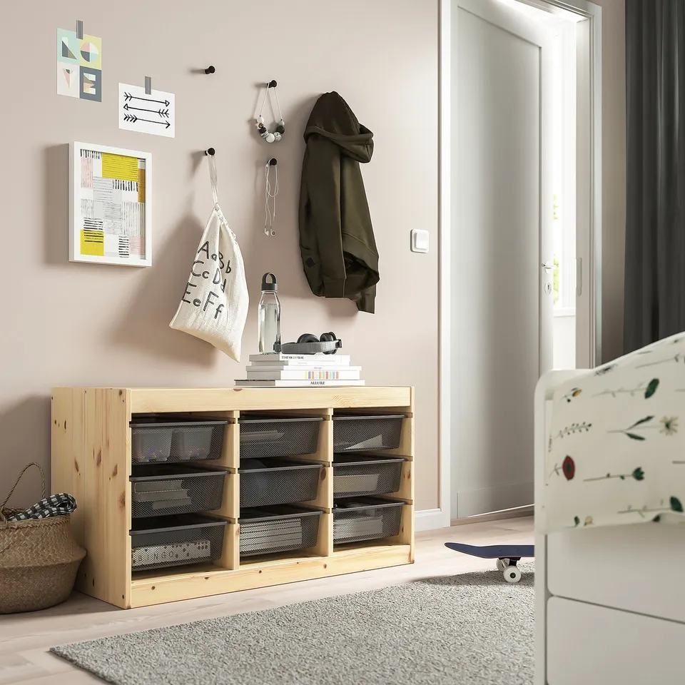 TROFAST wood storage with mesh drawers in kids room, holding books, a bottle, and a jacket. Skateboard nearby.