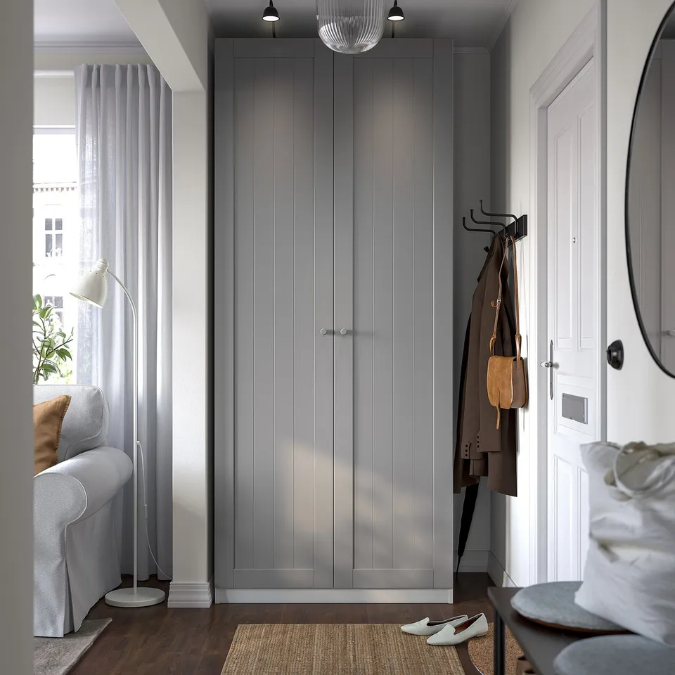Modern hallway with large grey wardrobe, coat rack, bench, mirror, and partial living room with sofa.