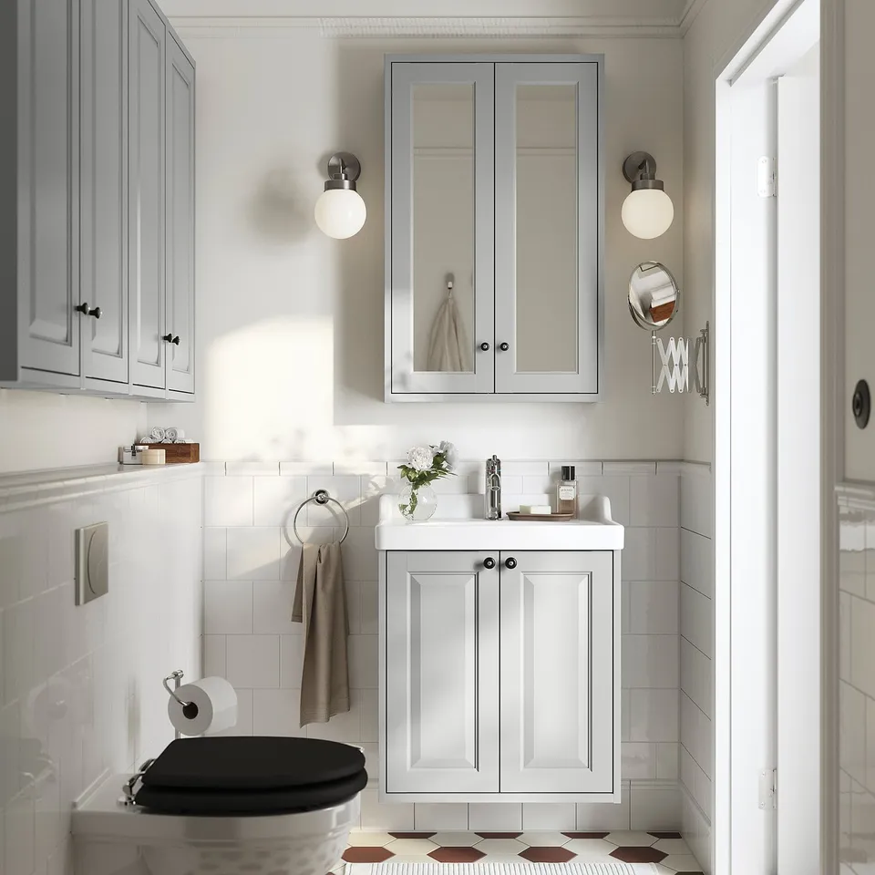 Modern bathroom with grey RUTSJÖN cabinet, oval sink, mirror cabinet, round lights, and black/white floor tiles.