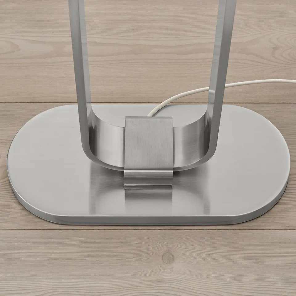 Base of modern metallic floor lamp, shiny and sleek, placed on wooden surface.