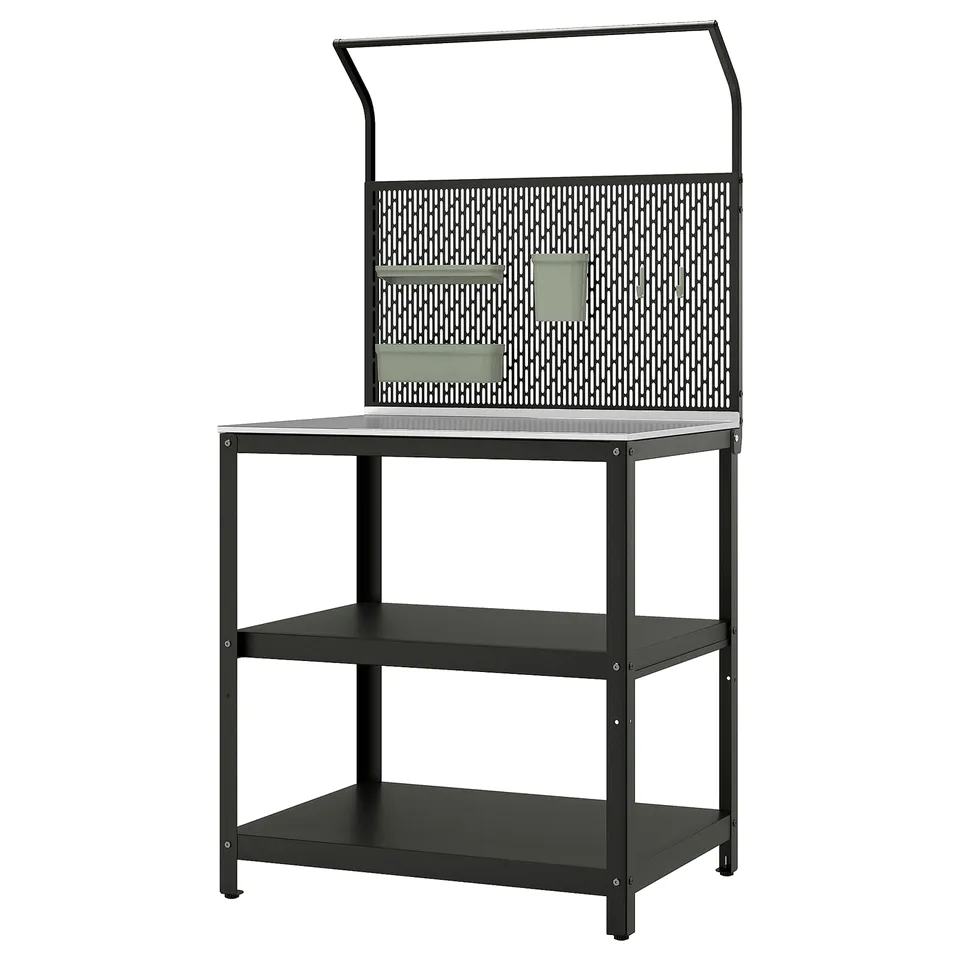 An ikea GRILLSKÄR outdoor kitchen island, black with a stainless steel top and perforated metal back panel. It has two lower shelves for storage.