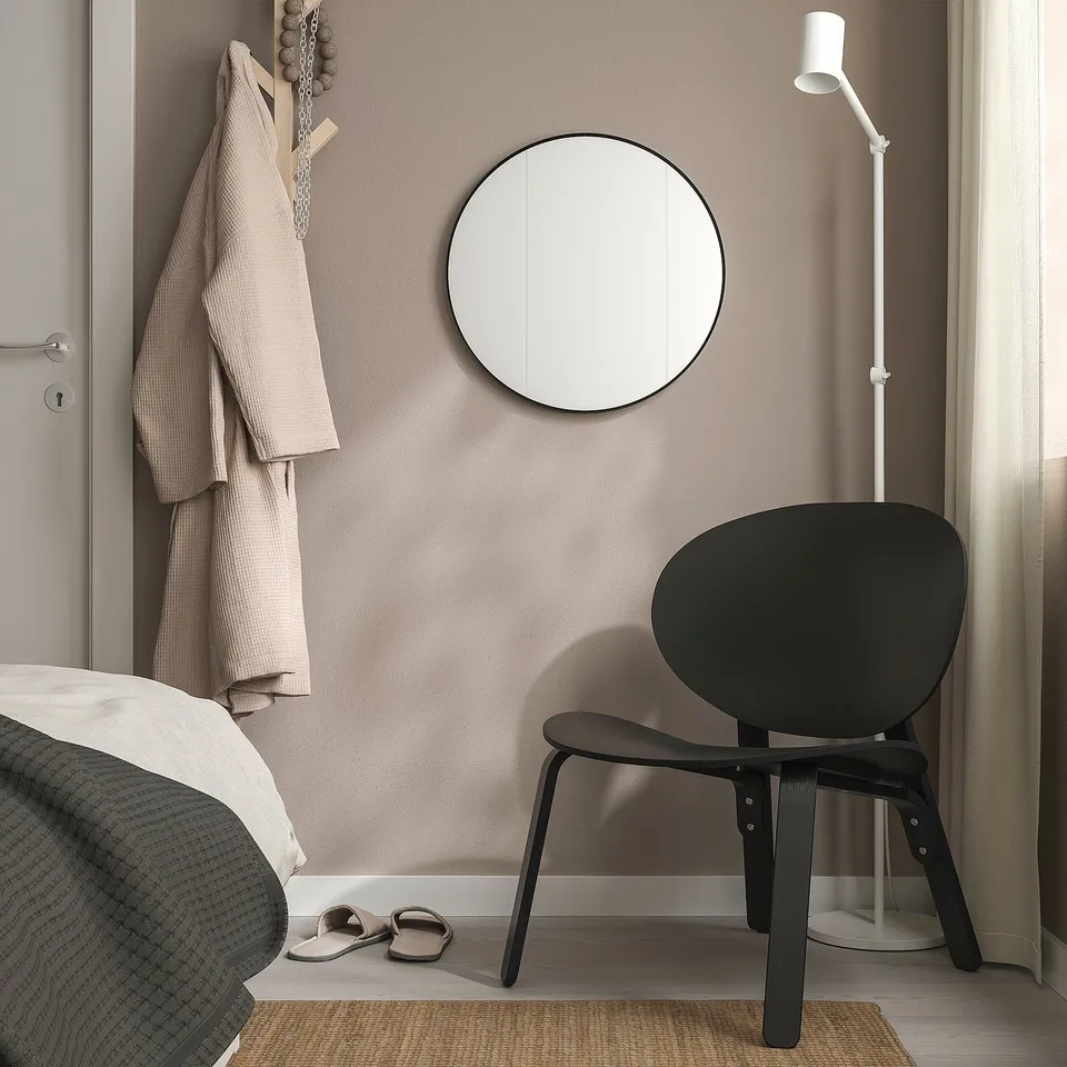 Modern bedroom with large LINDBYN mirror, black chair, and beige robe.