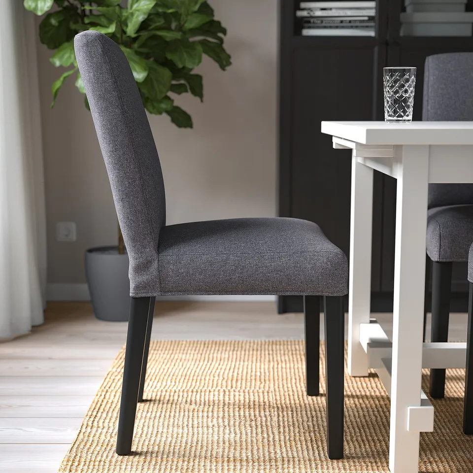 Dark grey upholstered dining chair with wooden legs on woven rug near white table.