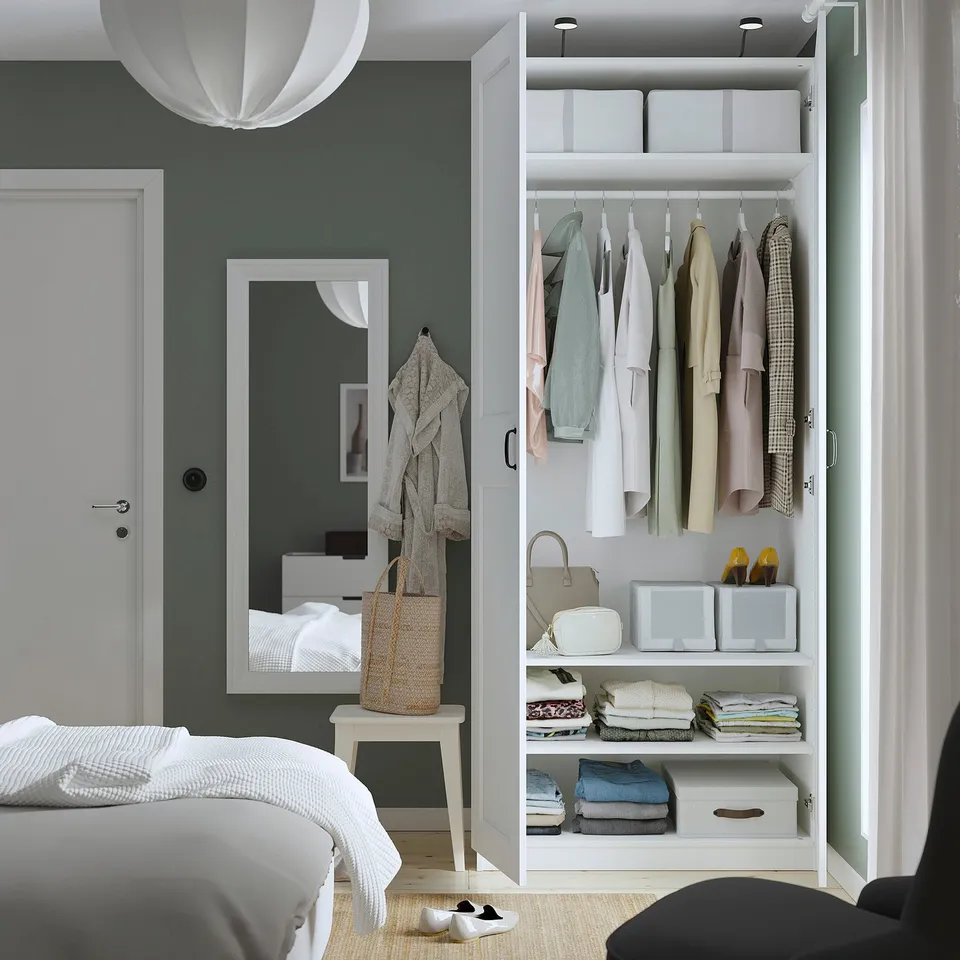 Modern bedroom with white PAX wardrobe, mirror, and bed with linens.