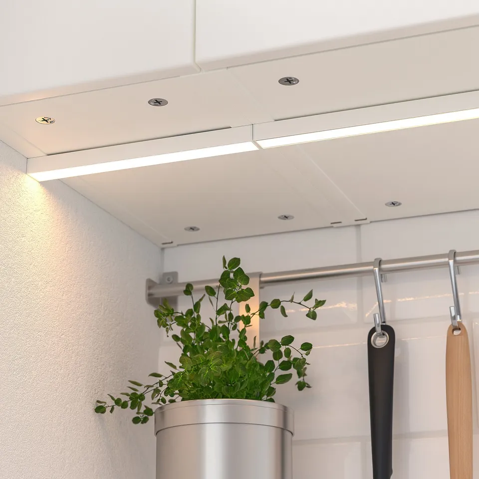 Kitchen under-cabinet lights mounted to ceiling, illuminating workspace. Plant and utensils visible below.