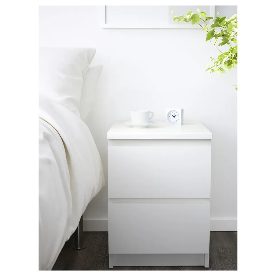 A white MALM bedside table with a cup and clock. Its small and matches the beds modern, clean design.