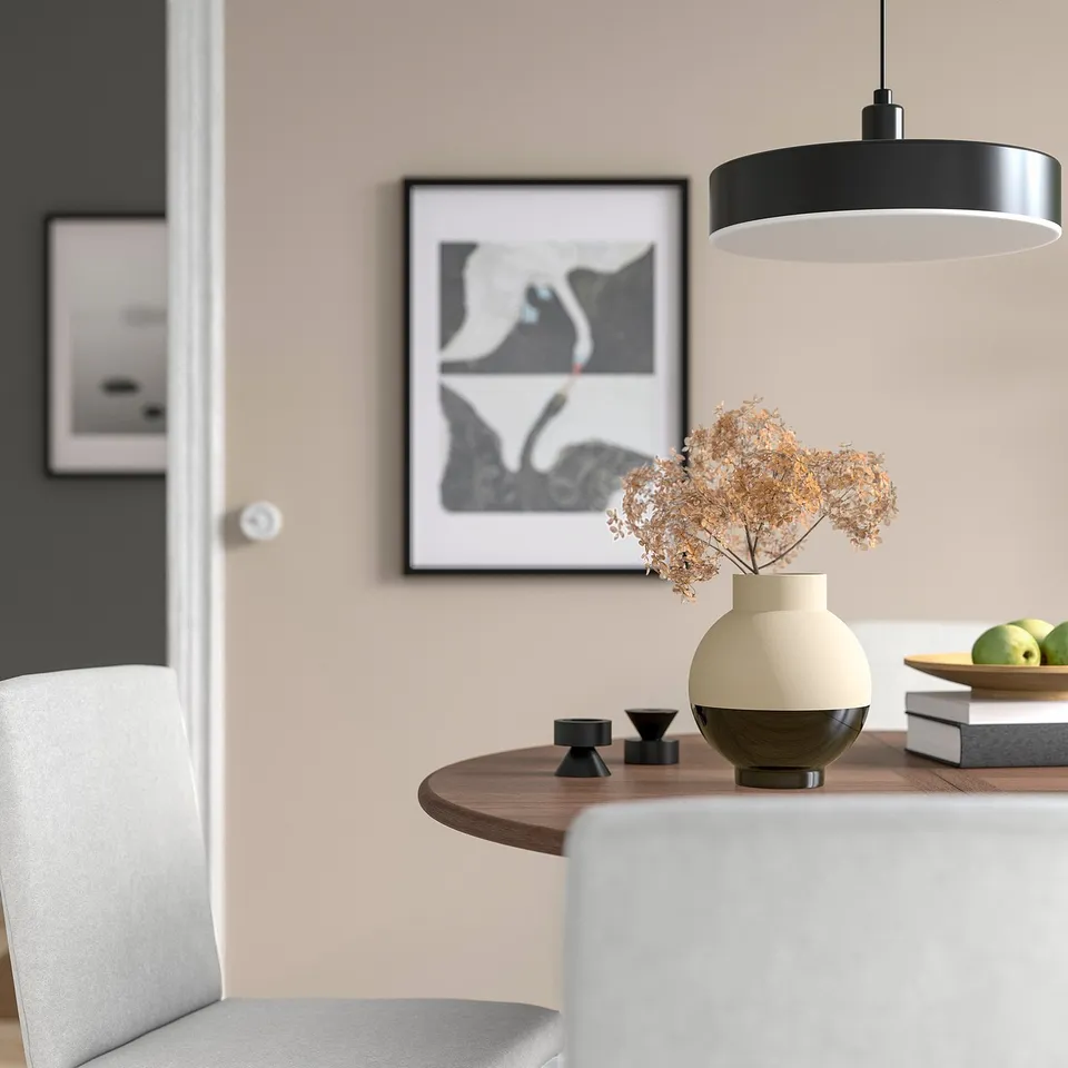 Modern dining table with black & beige vase, dried flowers, small candle holders, green apples, pendant light, & abstract wall art.