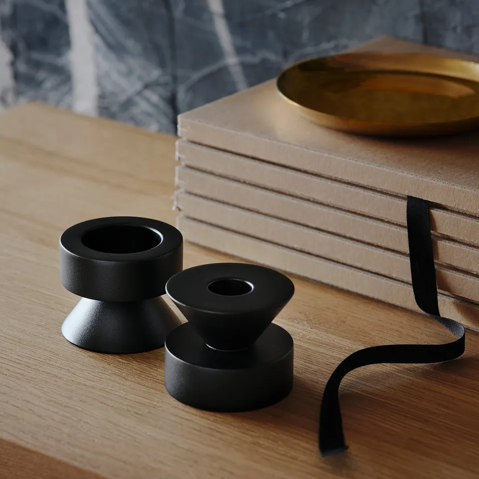 Black metal candlesticks on wood table, with books and gold dish.