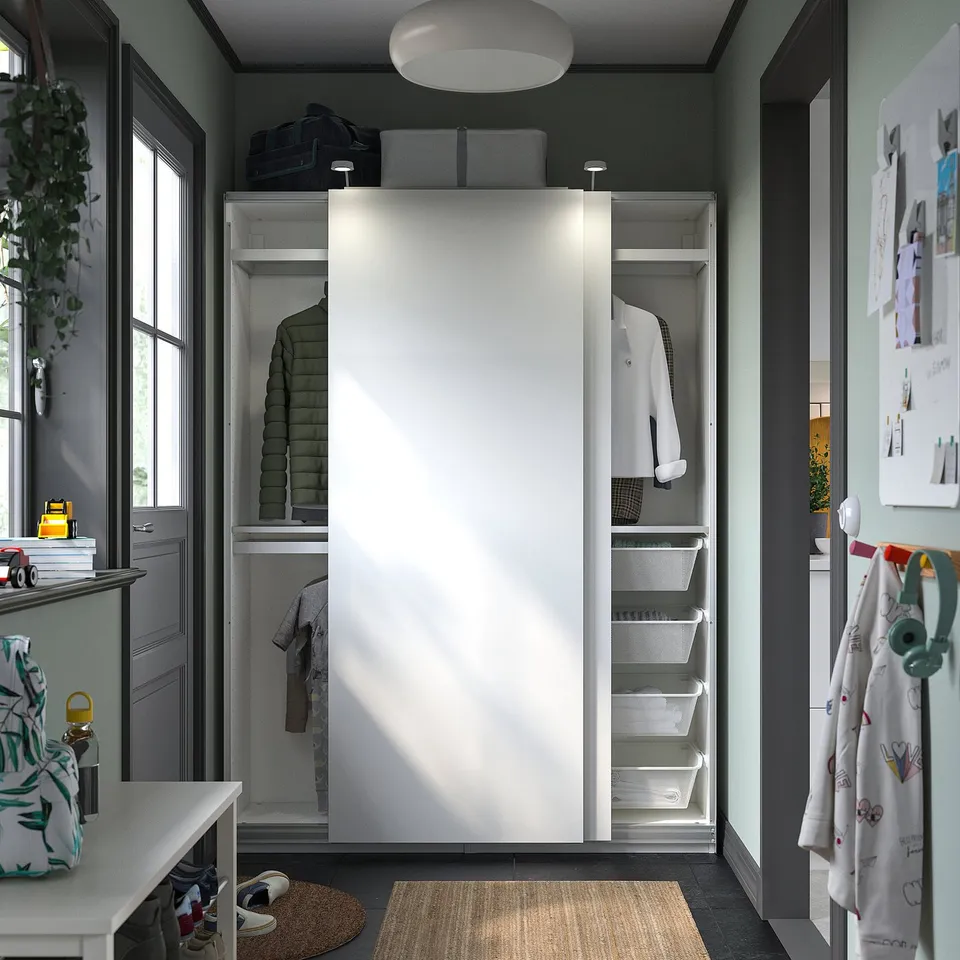 Modern closet with sliding doors, storage shelves, and white bins. Plant and hanging coats nearby.