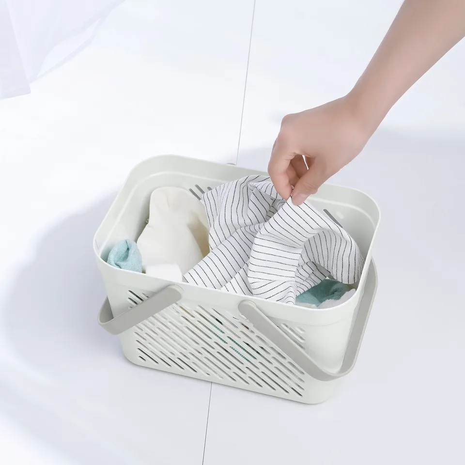 Person placing items into a white RÅNEN shower storage basket. The basket has holes for ventilation and is used for organising bathroom essentials.