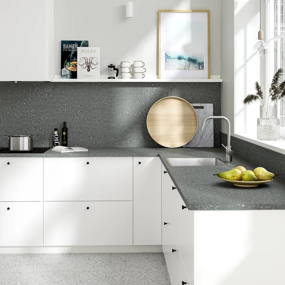 Modern kitchen with grey speckled countertop, white cabinets, and green apples.