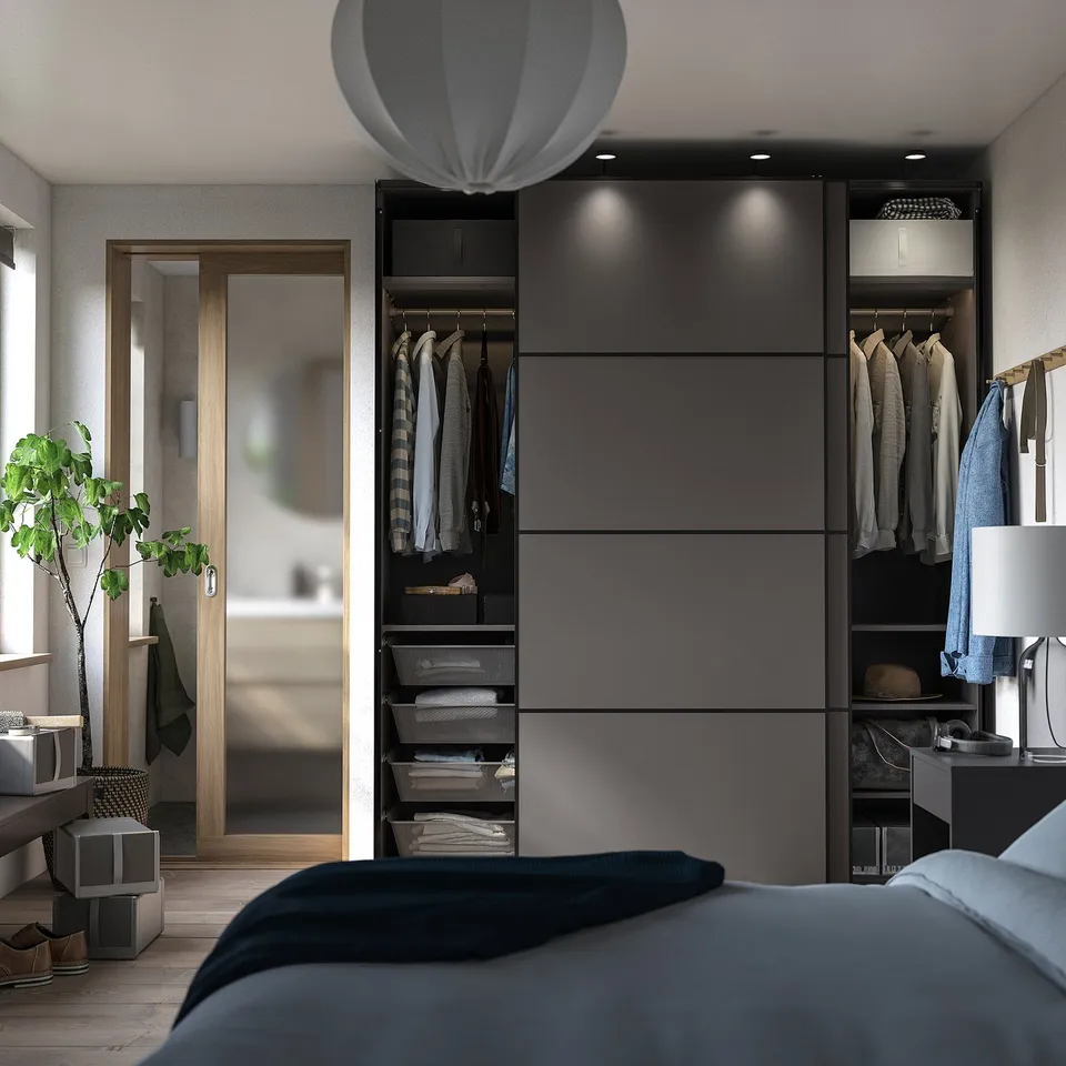 Modern bedroom with grey PAX wardrobe, sliding doors, mirror, and plant reflection.