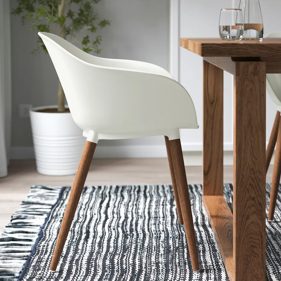 Modern dining area with white chairs and a wooden table on a striped rug, showcasing easy-to-clean seats and sturdy legs.