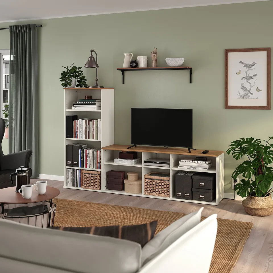 Modern living room with SKRUVBY tv stand & bookshelf. Green walls, white furniture, wooden accents. Tv centred, books, & plants.