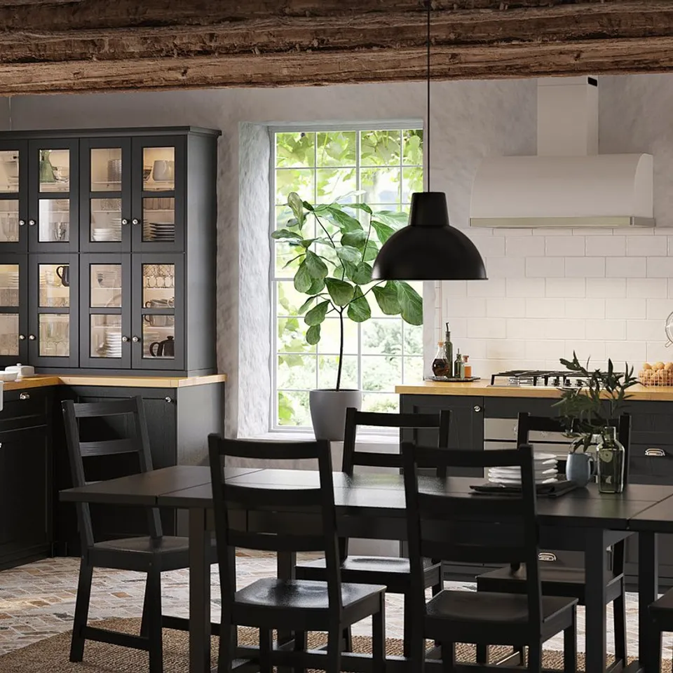 Modern kitchen with black METOD cabinets, stainless appliances, white tiles, wooden table, chairs, and hanging lights.