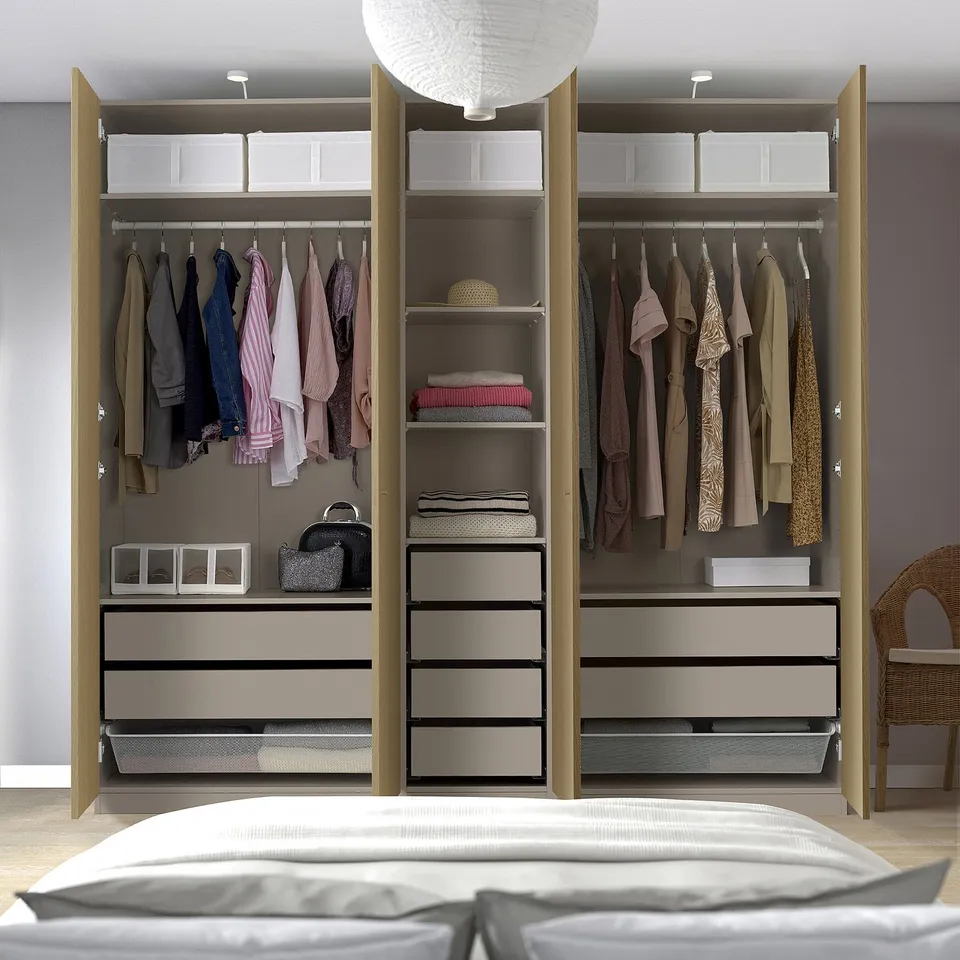 Tidy bedroom with open wardrobe showing clothes, shelves, drawers, and accessories in white and wood tones.