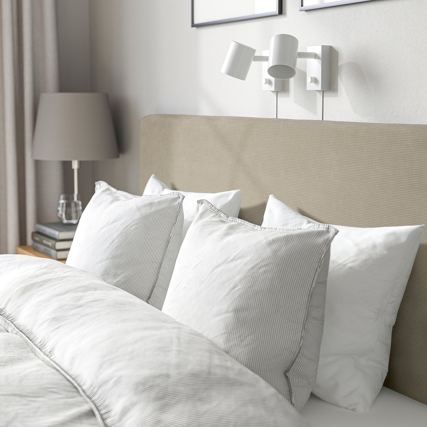 Bed with soft, padded headboard, white linens, wall lights, and bedside table with lamp, books, and water glass.