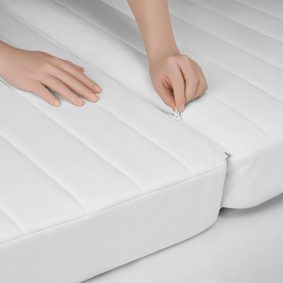 Close-up: hands zipping a clean, heavily textured white mattress. Quality fabric, well-made.