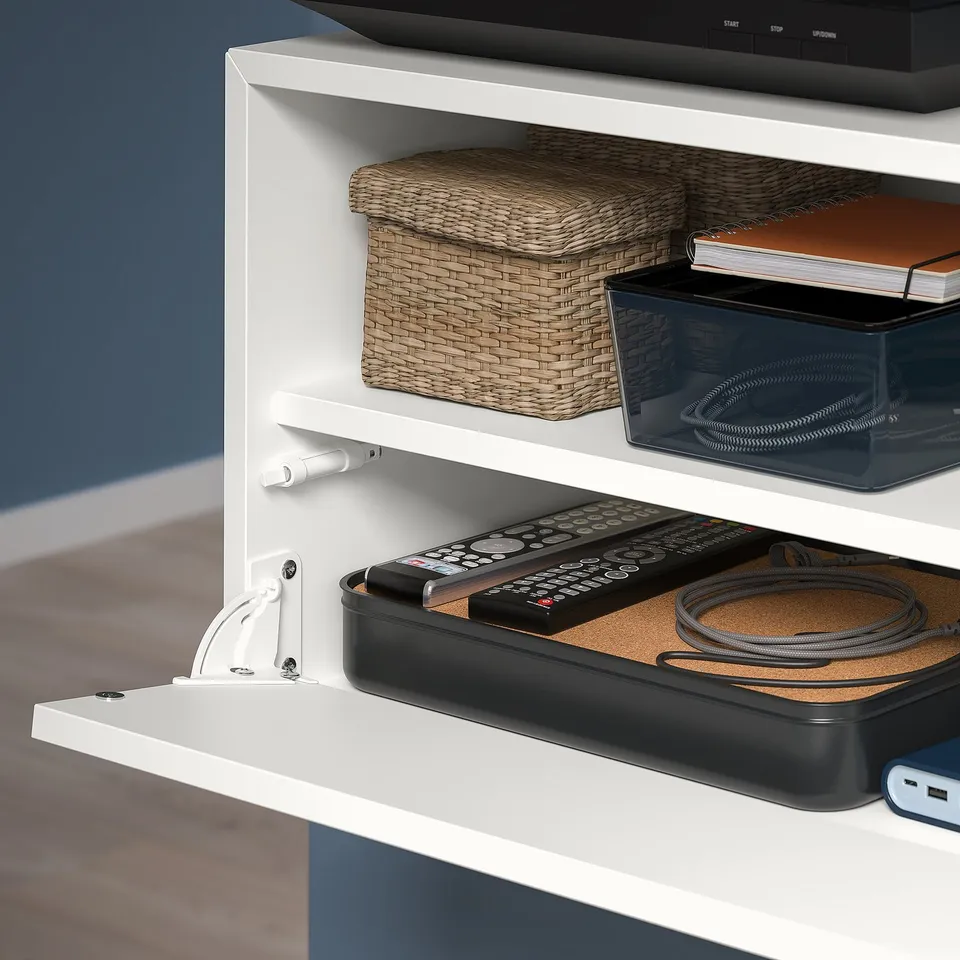 White EKET wall storage with flip-down media shelf, organising remotes and cables.