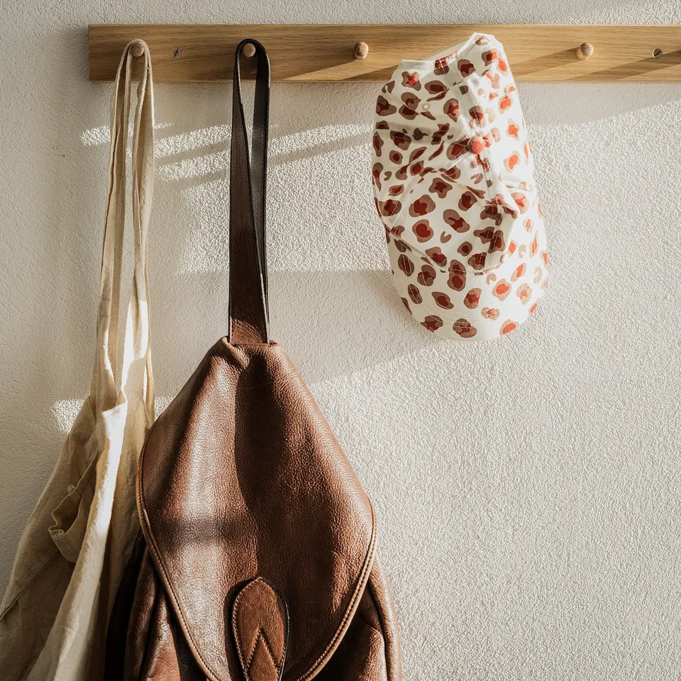 Leather bag and patterned face mask hang on wooden rack.