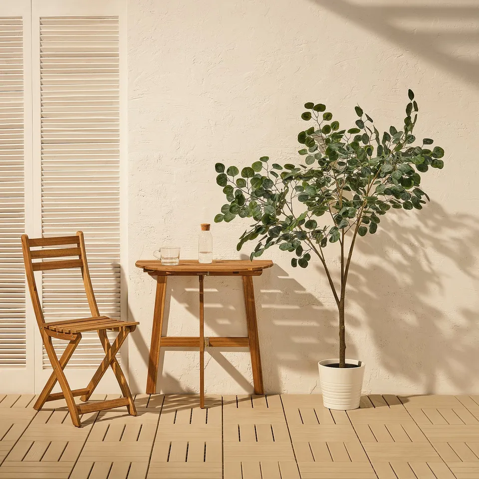 Small wooden patio set with a folding chair and table, perfect for outdoor relaxation. Beside it, a potted FEJKA artificial plant adds natural beauty.