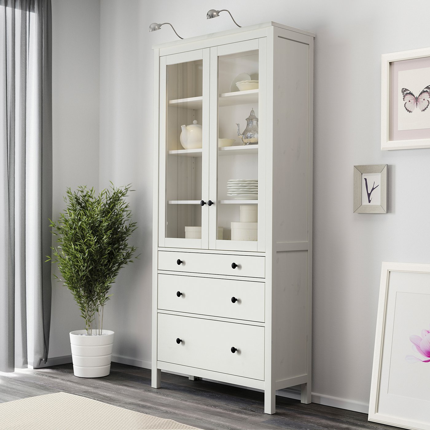 A white wooden cabinet with glass doors displaying dishes; it includes drawers for hidden storage.